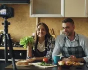 Young attractive couple shooting video food blog about cooking on dslr camera in the kitchen at home